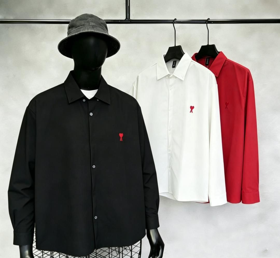 Black shirt on mannequin beside white and red AMI embroidered button-up shirts