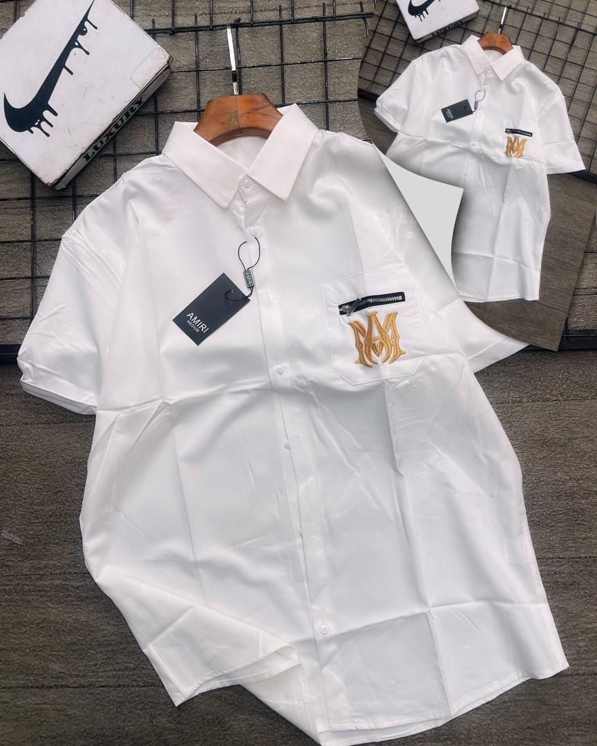 White AMURI short sleeve shirt with gold MM embroidery on zip pocket, shown on wooden hanger.