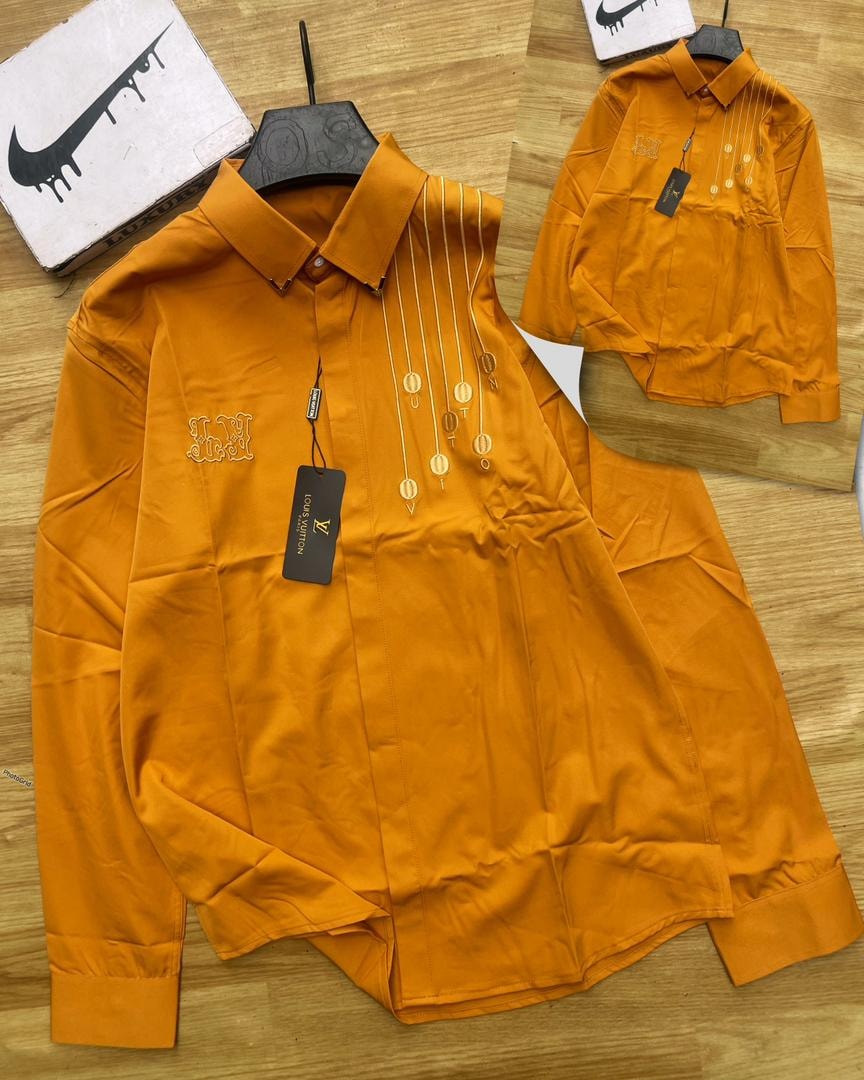 Orange Louis Vuitton embroidered long sleeve shirt with hanging medallions and tags.