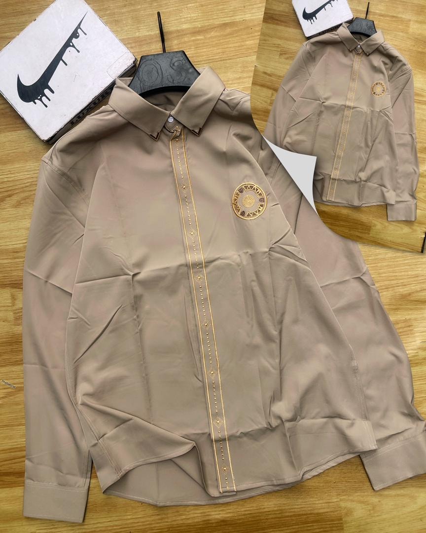 Beige luxury corporate shirt with gold placket trim and circular chest emblem.