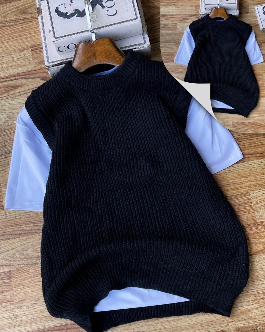 Black ribbed knit armless cardigan layered over white t-shirt on wooden surface.