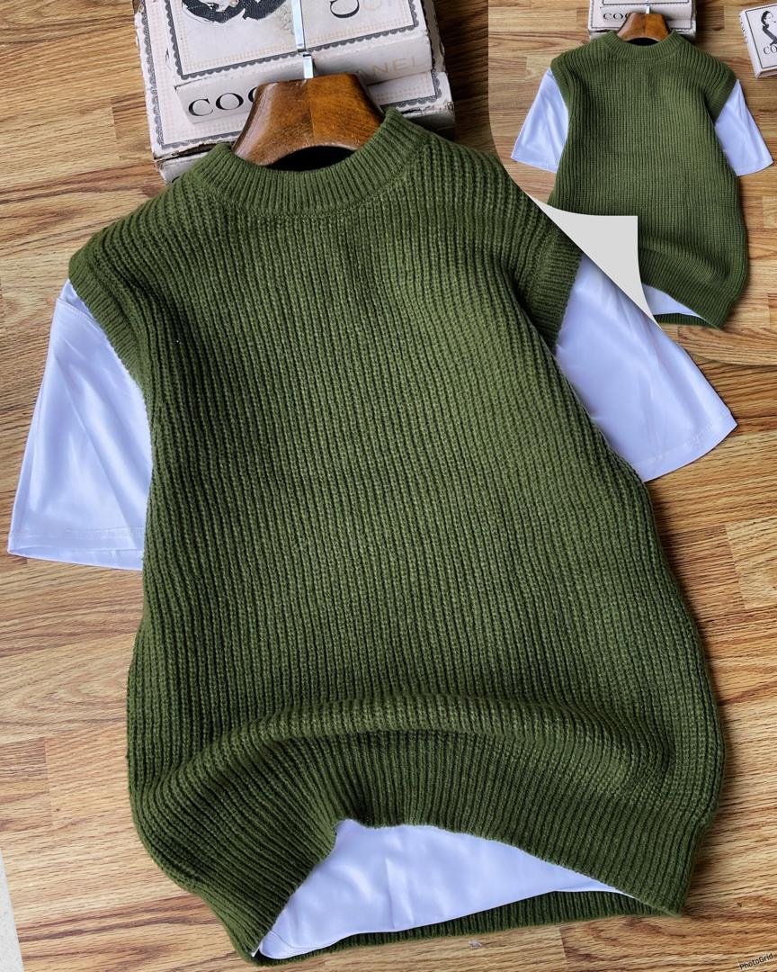 Olive ribbed knit armless cardigan layered over white t-shirt on wooden surface.