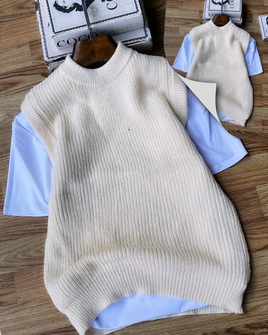 Cream ribbed knit armless cardigan layered over white t-shirt on wooden surface.