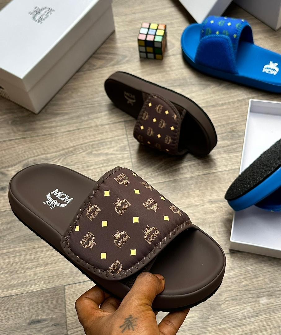Brown MCM monogram slide with gold logos held in hand with packaging around.