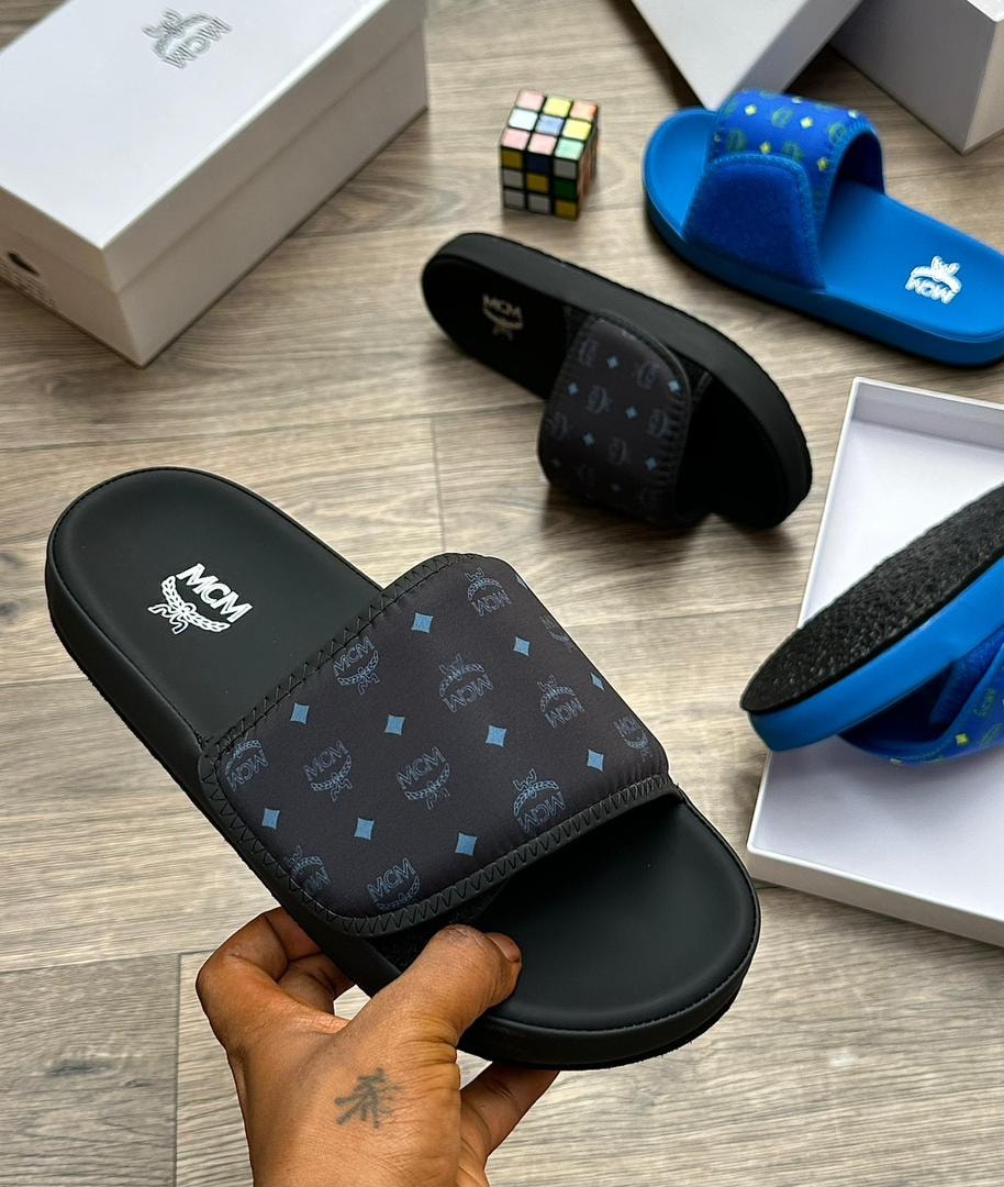 Black MCM monogram slide with blue diamond accents held in hand.