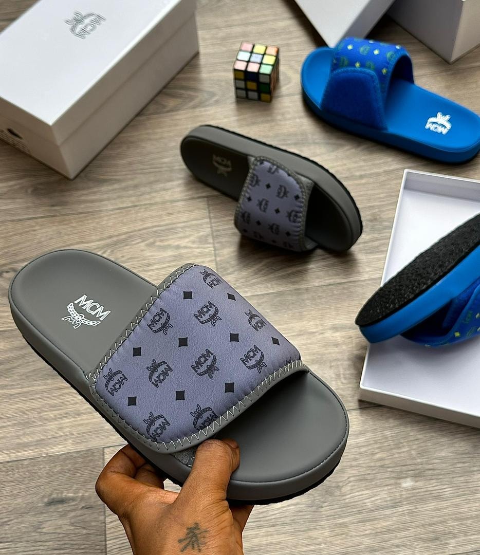 Gray MCM monogram slide with black logos held in hand, additional slides in background.