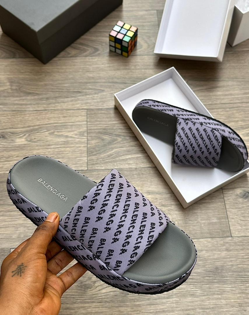 Balenciaga all-over logo printed slide in gray held in hand showing detailed text pattern.