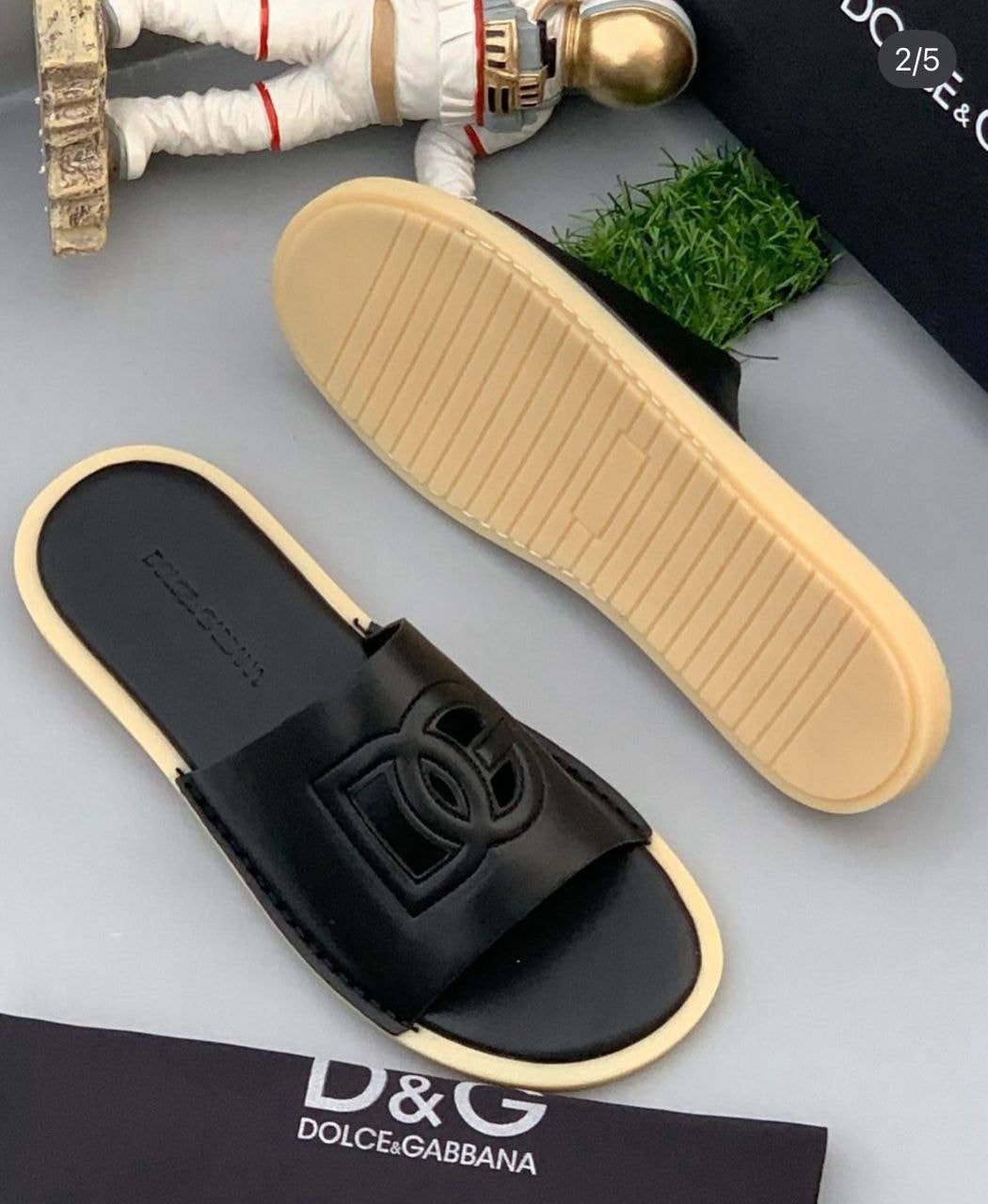 Black Dolce & Gabbana slide with embossed logo on strap, shown from top and bottom angles with accessories and branding.