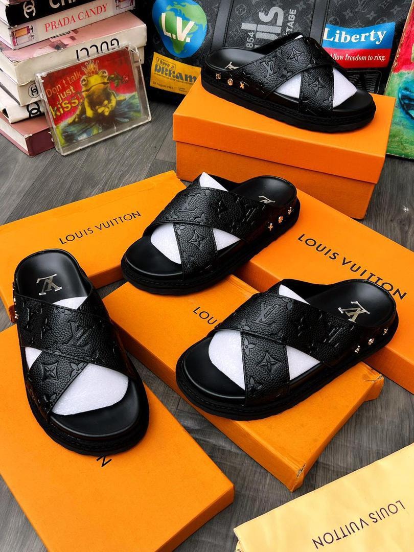 Black Louis Vuitton monogram slides arranged on orange boxes with branded accessories and books.