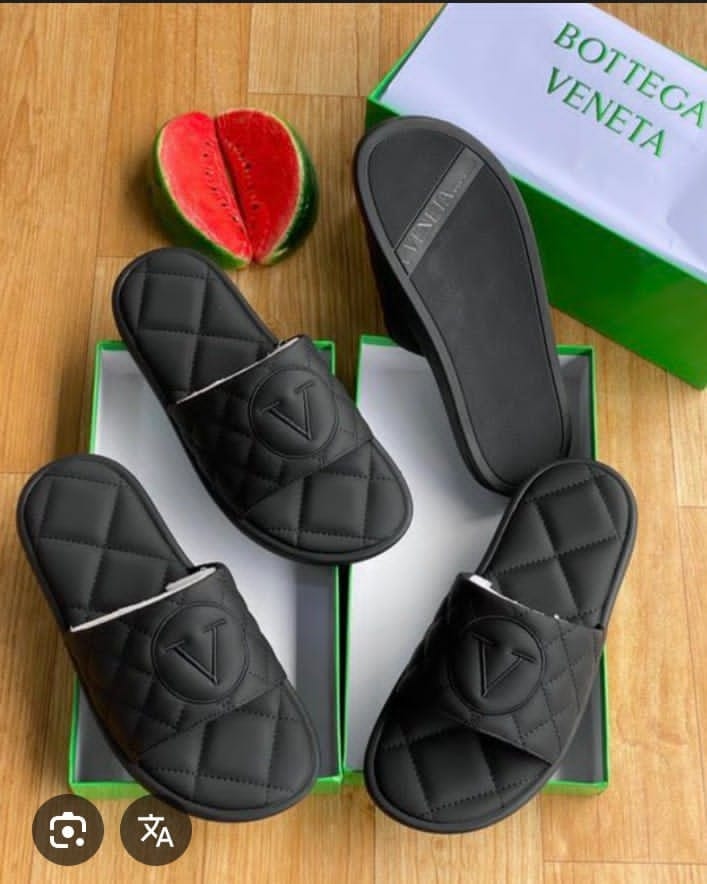 Black quilted slides with V logo displayed on green box with watermelon prop and Bottega Veneta packaging.