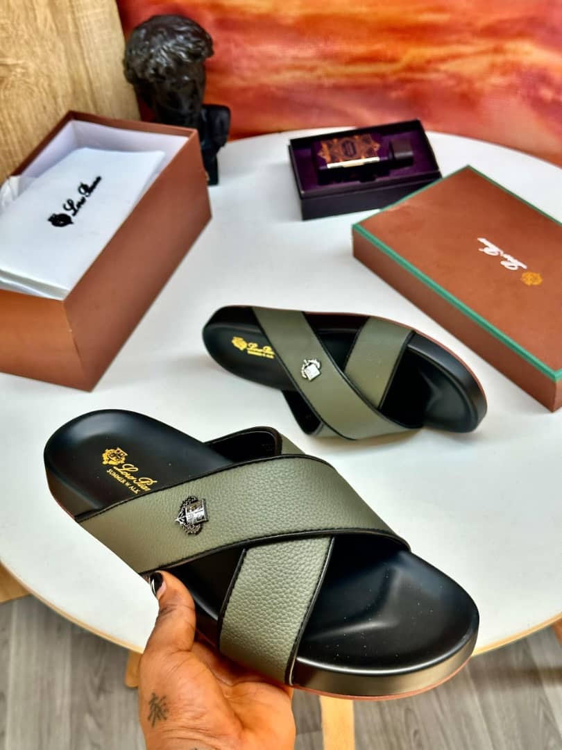 Olive green cross-strap slides held in hand with luxury boxes and perfume in background.