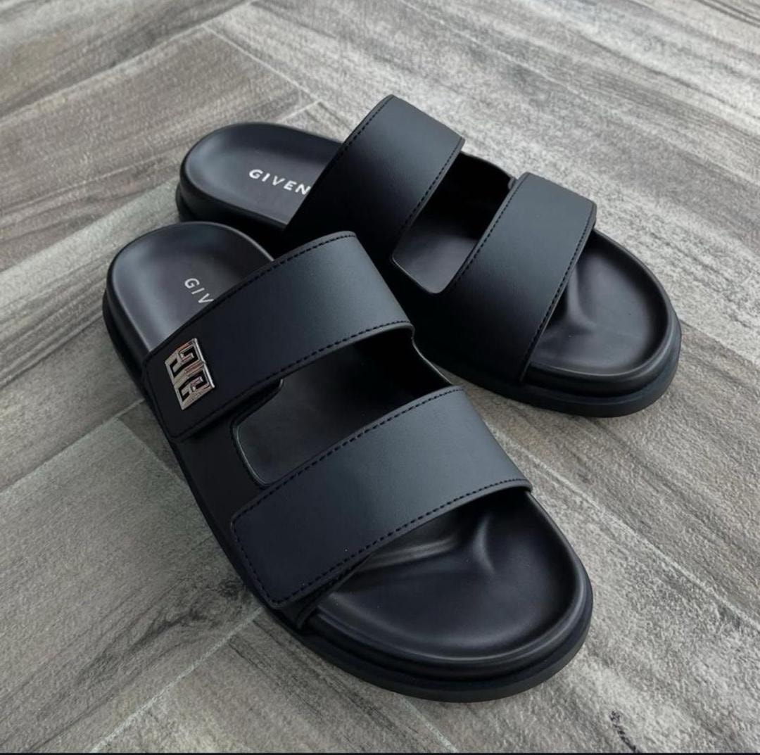 Black Givenchy double-strap slides with metal logo on gray wood floor.