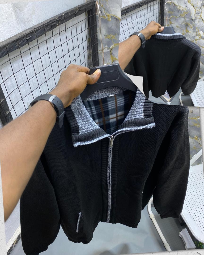 Black knitted full-zip sweatshirt on hanger showing textured fabric, striped collar and plaid interior lining.