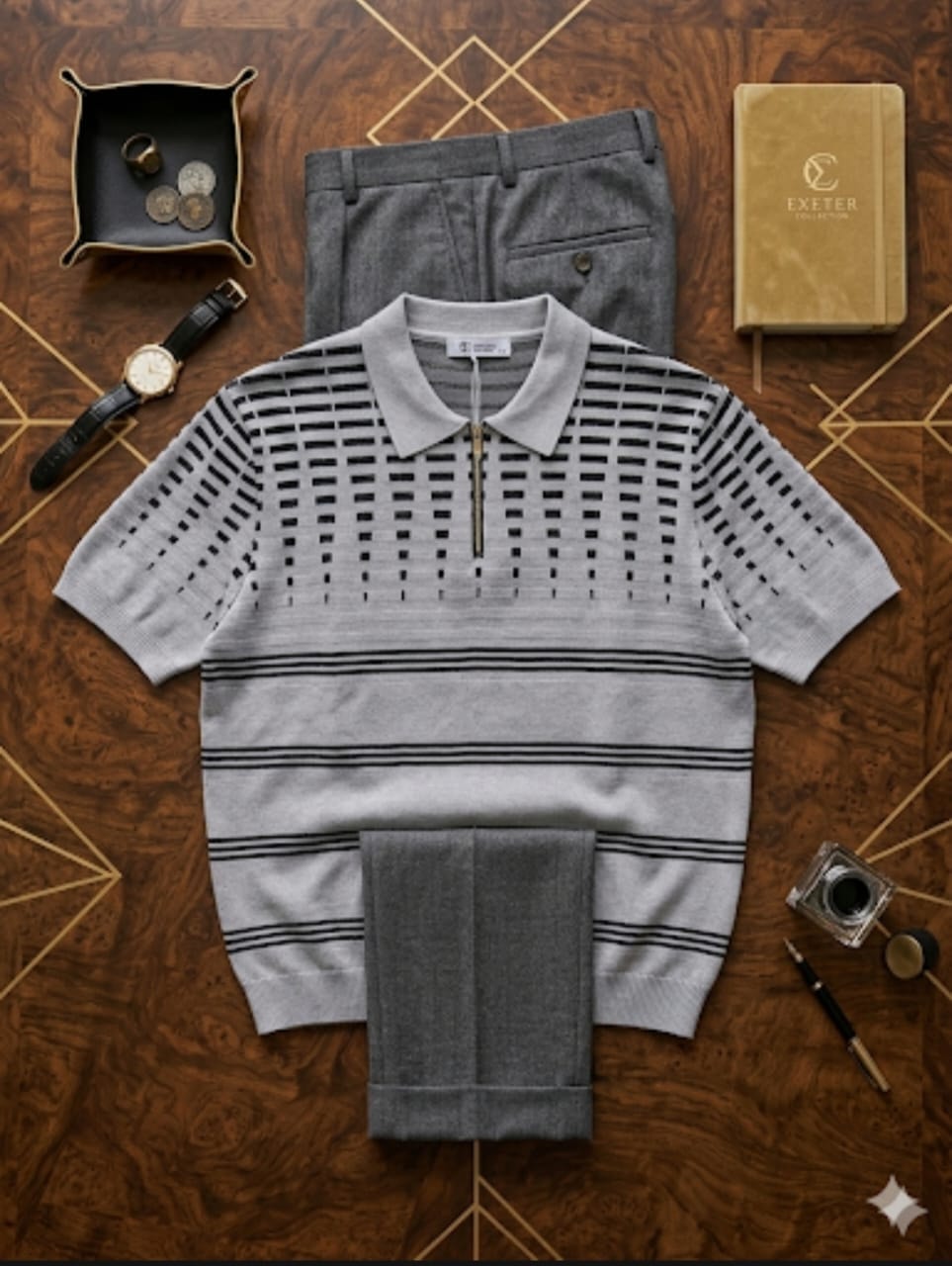Grey and black striped knit polo with grey trousers displayed flat with watch, tray and notebook accessories.