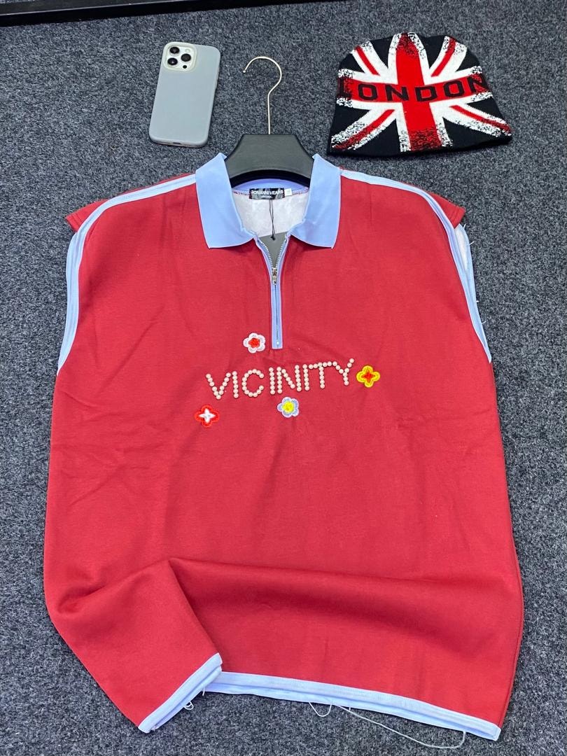 Red armless quarter-zip polo with VICINITY beaded text and flower embroidery.