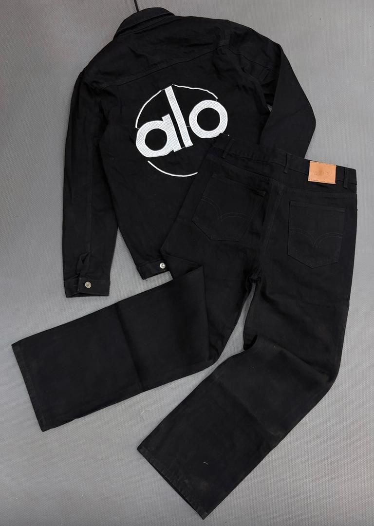 Black denim jacket with large white Alo logo on the back paired with matching black jeans on gray surface.