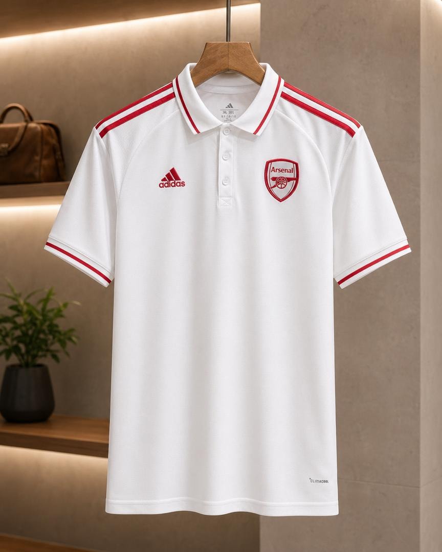 White Adidas Arsenal polo shirt hanging on wooden hanger with red trim.