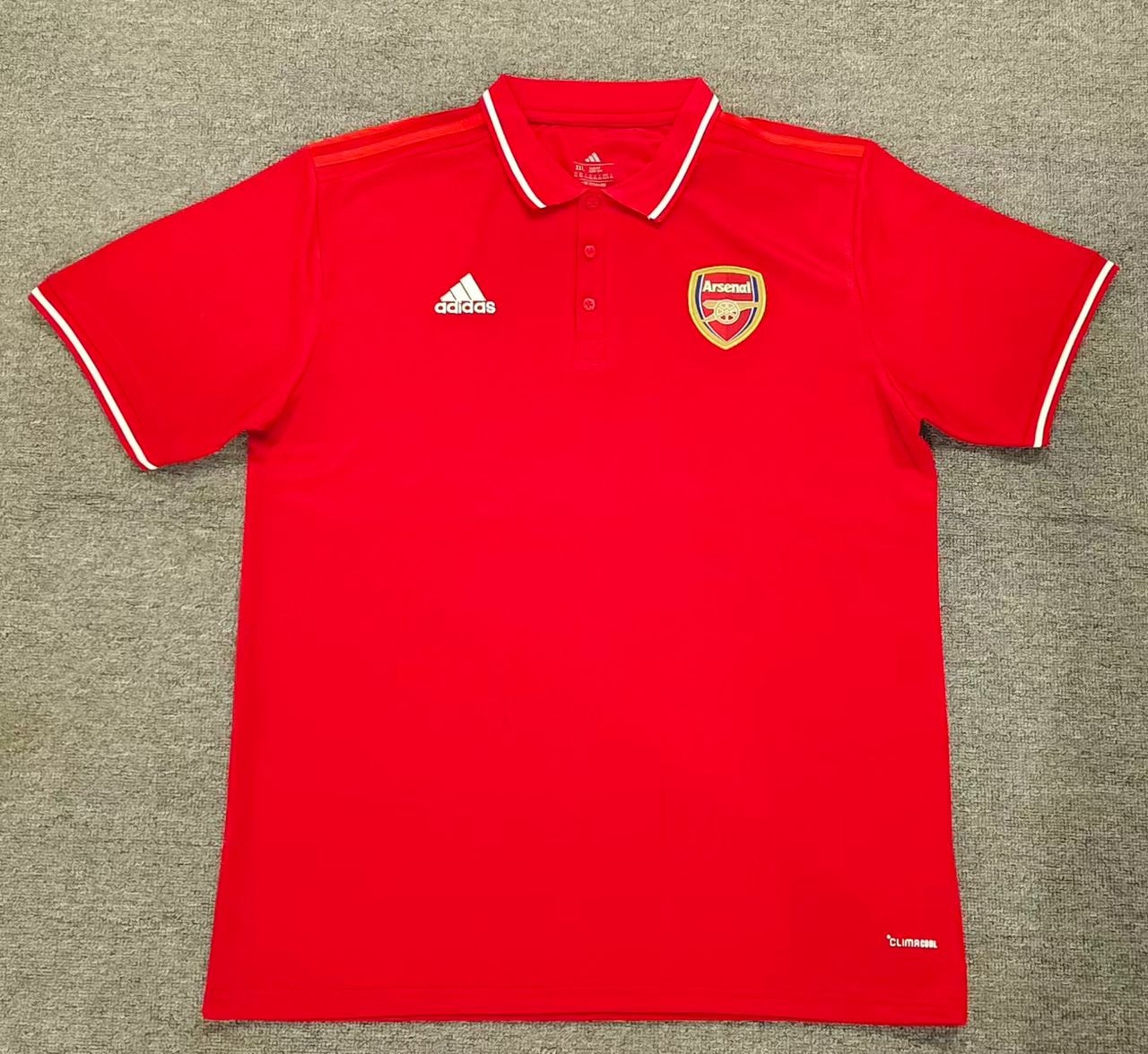 Red Adidas Arsenal polo shirt laid flat on gray surface.