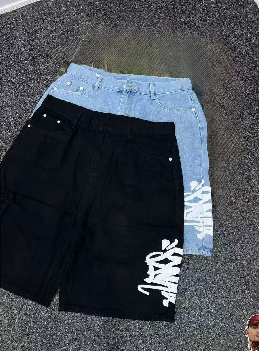 Black denim shorts with white graphic print layered with light blue denim pair on textured surface.