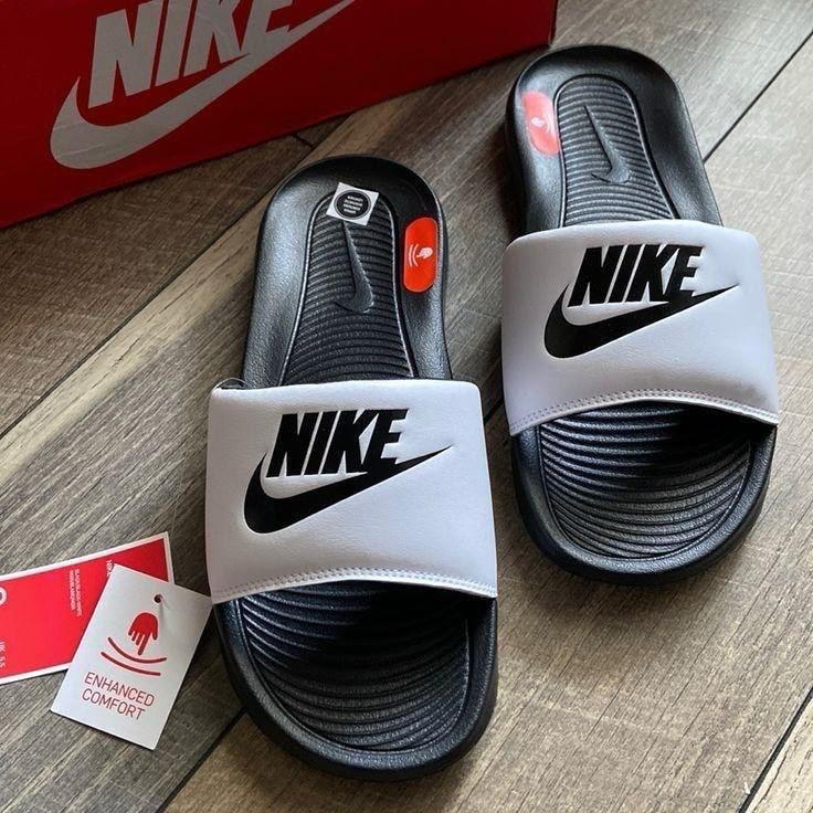 White and black Nike Victori One Slides with tags on wooden surface.