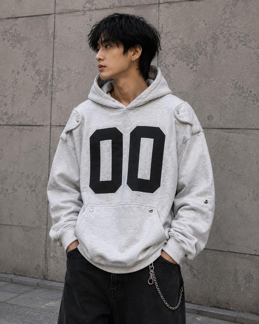 Man modeling light gray oversized hoodie with large black 00 graphic and shoulder buttons.