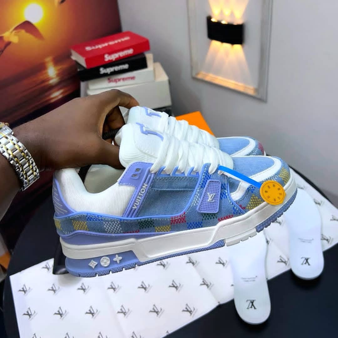 Blue Louis Vuitton checkered sneakers held showing side profile with LV monogram and accessories.