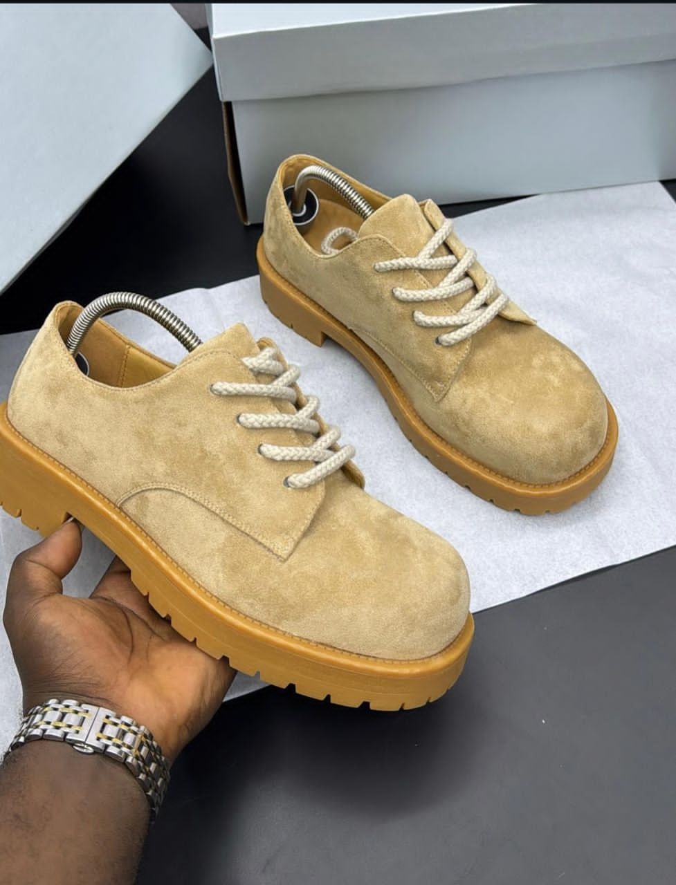 Hand holding tan suede chunky platform lace-up shoe to display profile and thick sole detail.
