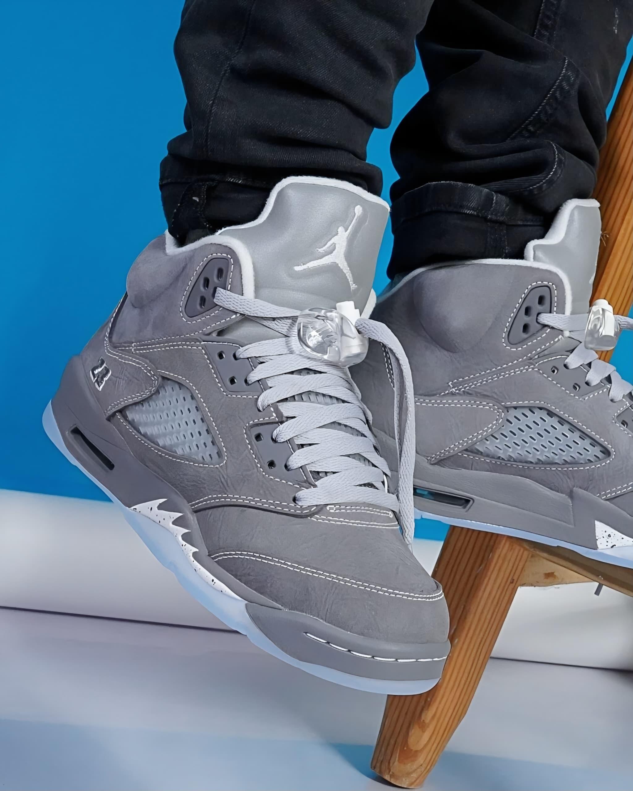 Gray Air Jordan 5 sneakers worn on feet against bright blue background.