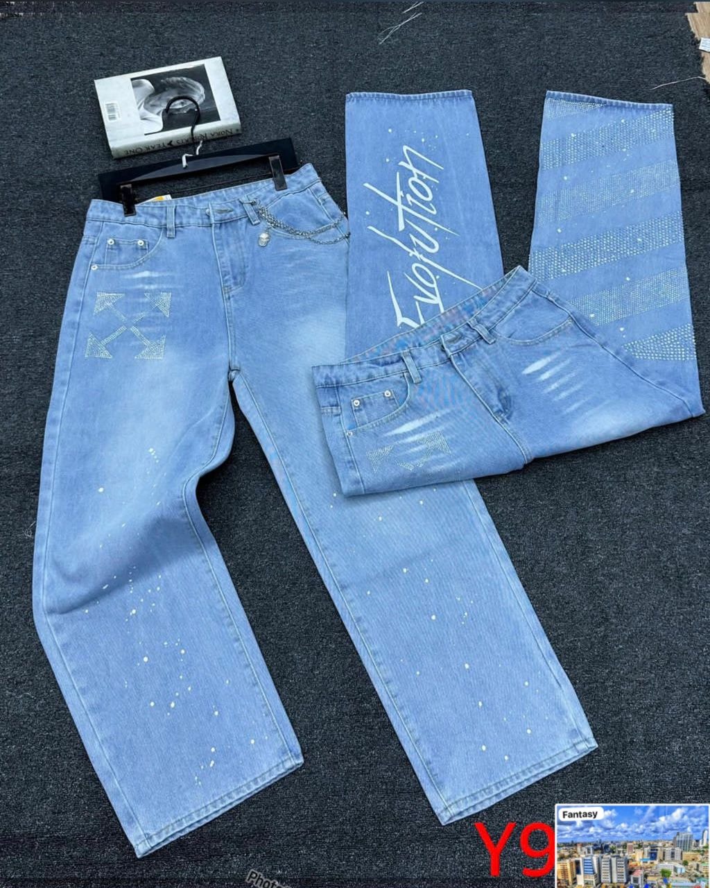 Light blue baggy jeans with rhinestone Evolution script, arrow designs and dot patterns laid flat.