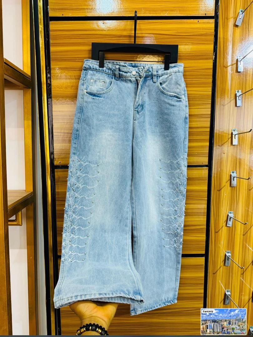 Light blue baggy jeans with white embroidery and pearl beading on legs, hanging display.