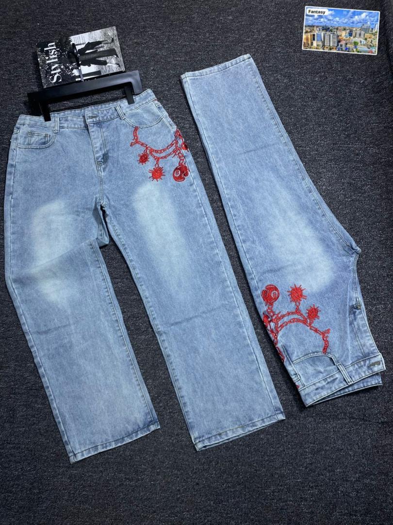 Light blue baggy jeans with red chain embroidery on pocket and leg, laid flat.