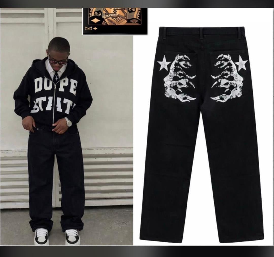 Model wearing black baggy jeans with hoodie beside close-up of back with white graphic prints on pockets.