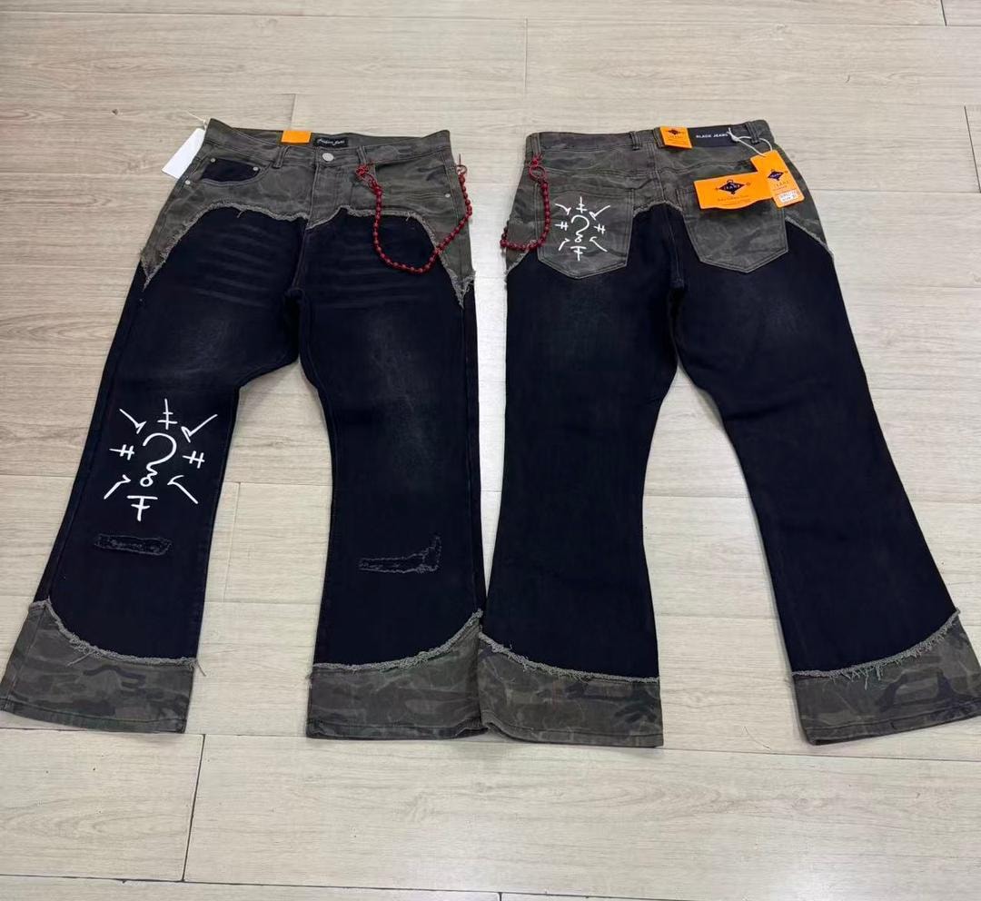Flat lay view of black baggy jeans with camouflage accents, white symbolic prints, and red beaded chain.
