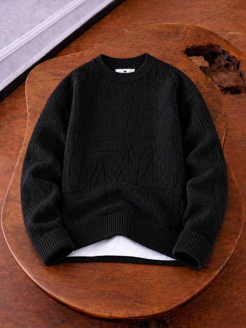 Black cable knit crewneck sweater laid flat on wooden surface.