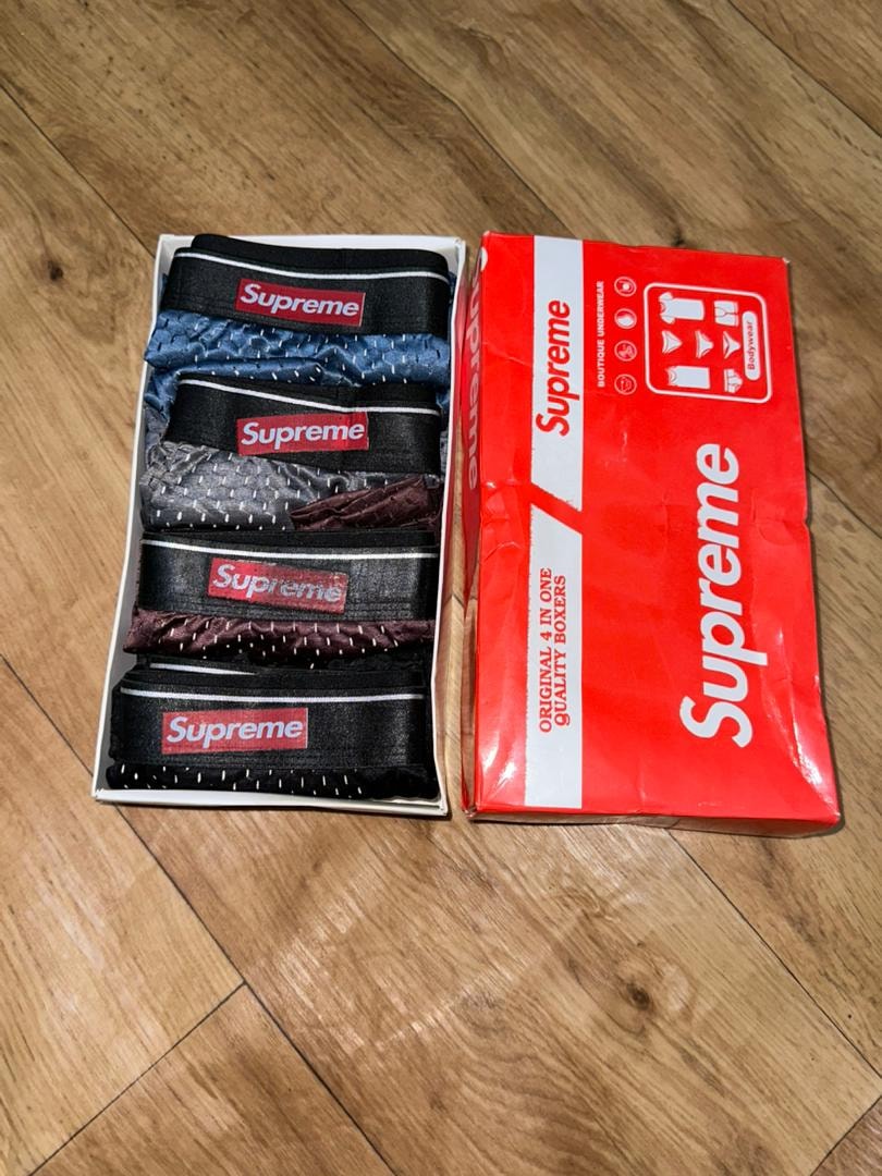 Supreme 4-in-1 quality boxers in white box next to red Supreme packaging on wooden floor.
