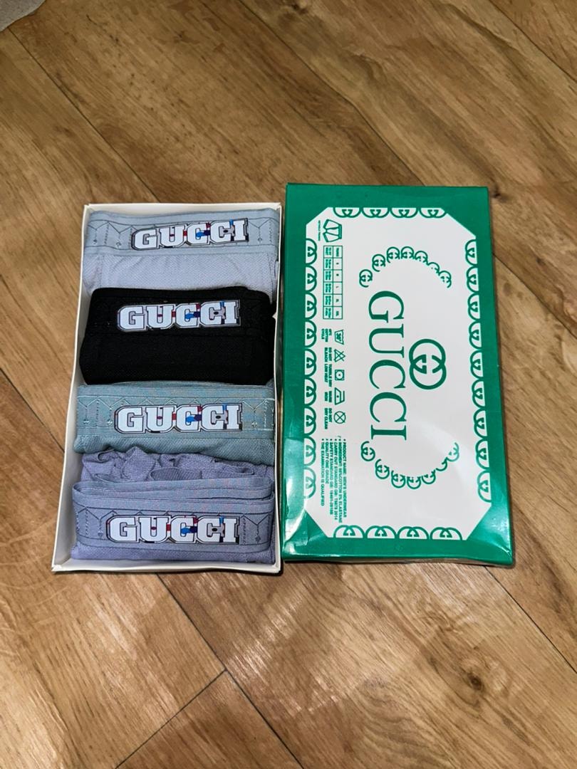 Gucci branded 4-in-1 boxers in open box alongside green Gucci packaging on wooden floor.
