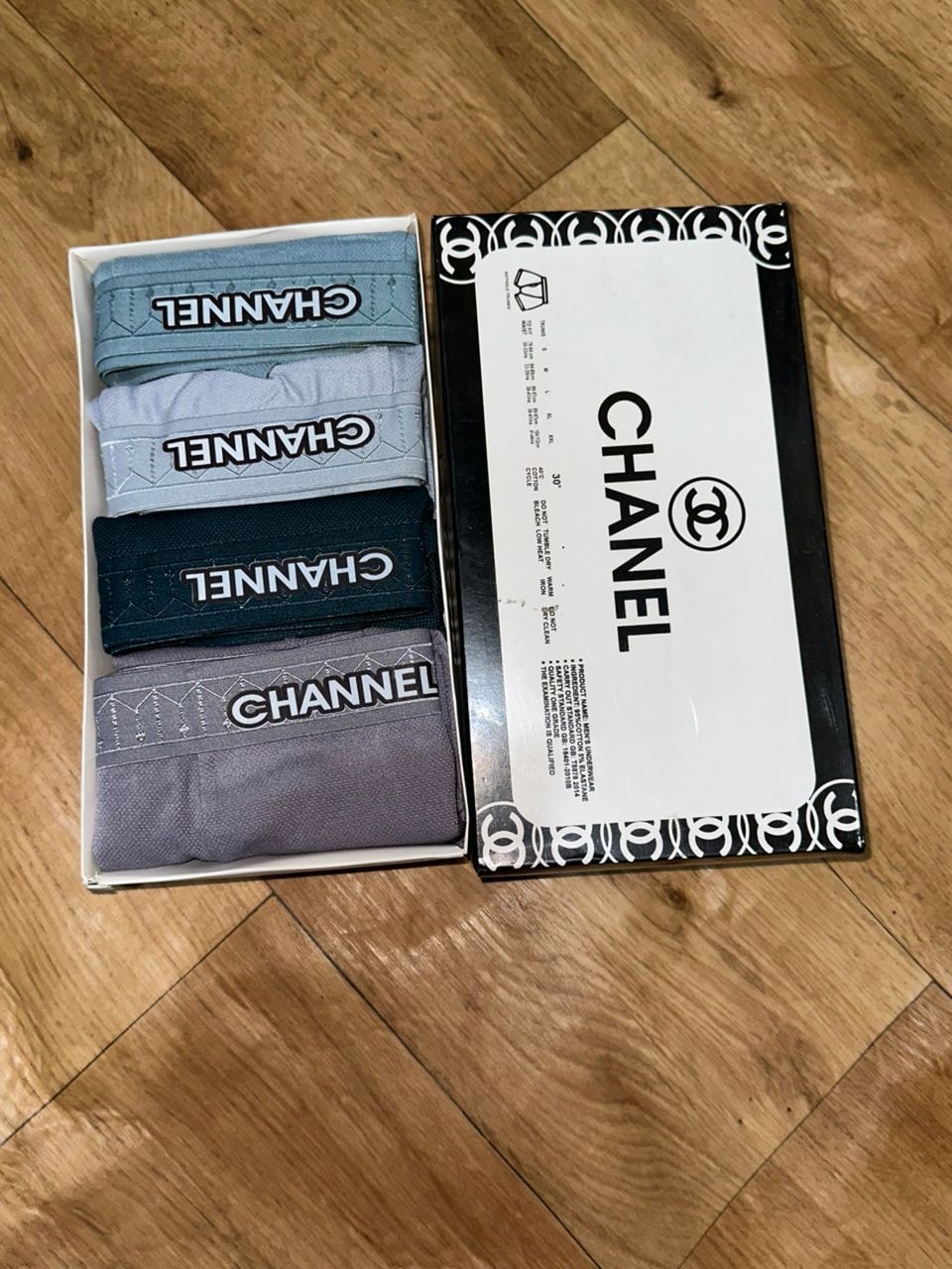 Chanel 4-in-1 boxer set displayed in open box next to black and white CC logo packaging on wooden surface.