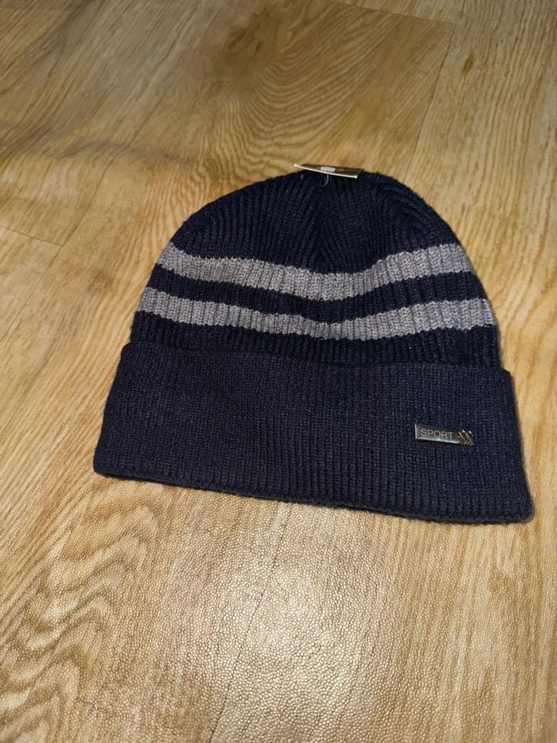 Navy blue knit beanie with gray stripes and SPORT label on wooden surface.