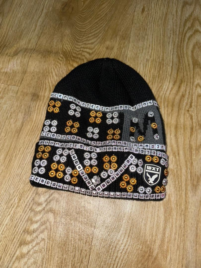 Black knit beanie with colorful patterns and WXT logo on wooden floor.