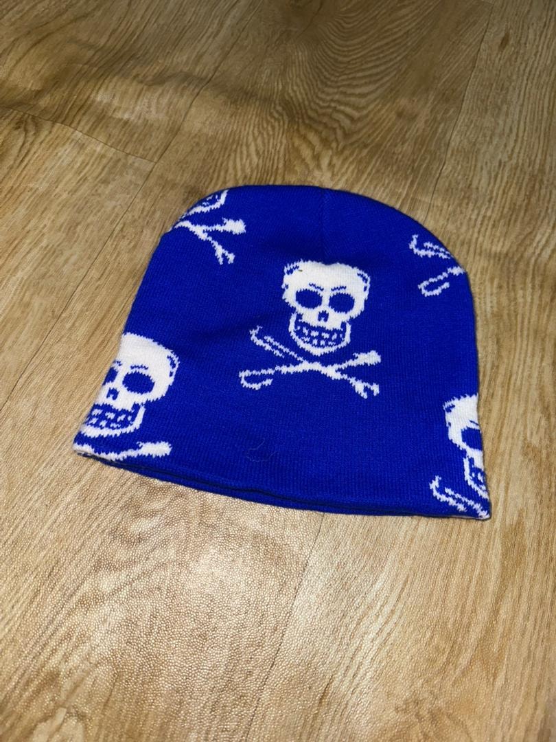 Blue skull and crossbones patterned knit beanie on wooden floor.
