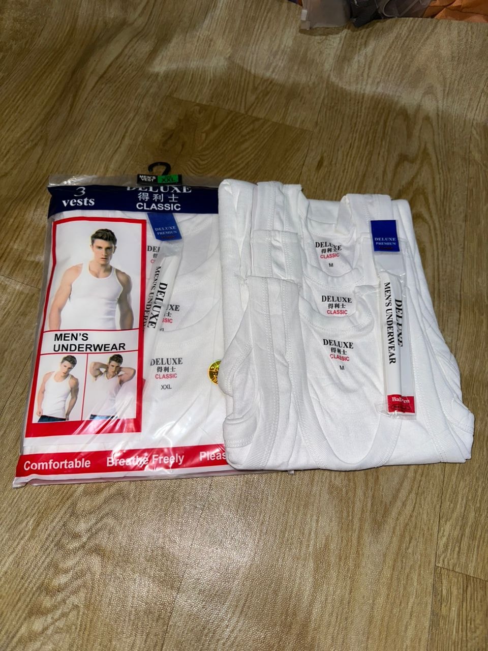 Deluxe Classic 3 vests packaging beside unfolded white men's tank tops showing M and XXL labels.