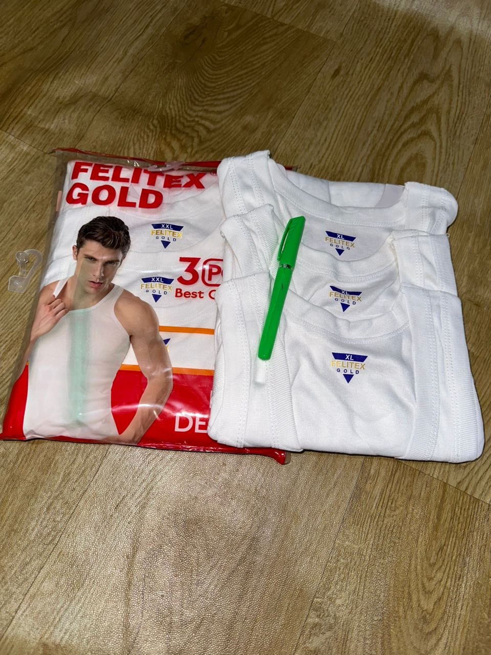 Unfolded Felitex Gold white XL singlets placed beside their 3pcs packaging with green marker for scale.