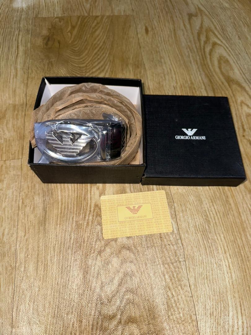 Giorgio Armani belt in black box with yellow authenticity card on wooden surface.