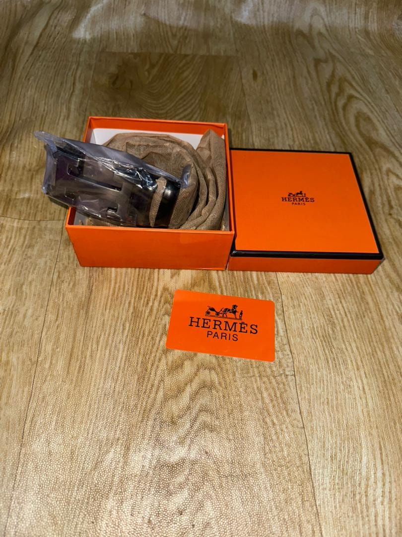 Hermes belt in orange box with orange Hermes authenticity card on wooden floor.