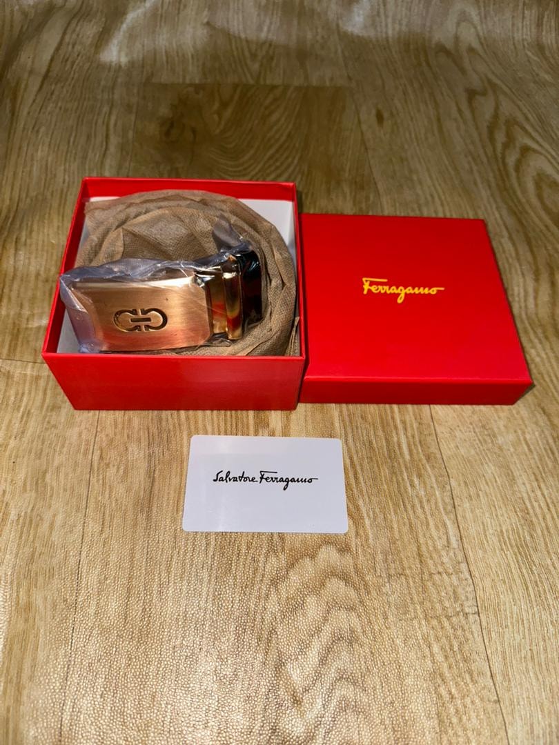 Ferragamo belt in red box with white Salvatore Ferragamo card on wooden surface.