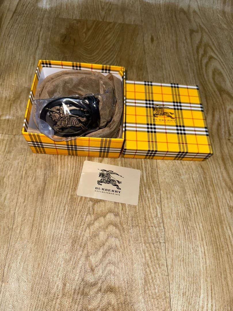 Burberry belt in yellow plaid box with beige authenticity card on wooden floor.