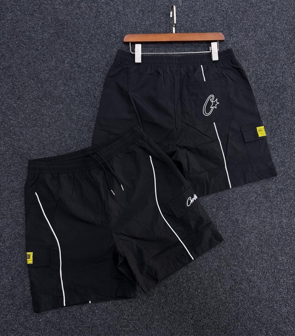 Black cargo shorts with white piping, flap pockets and script logo on hanger and flat lay.
