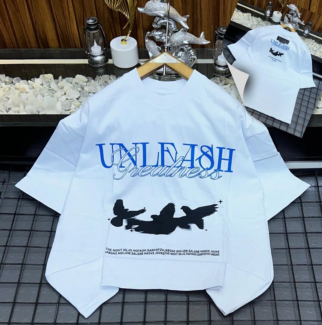 White Unleash Greatness oversized t-shirt with blue text and bird graphic.