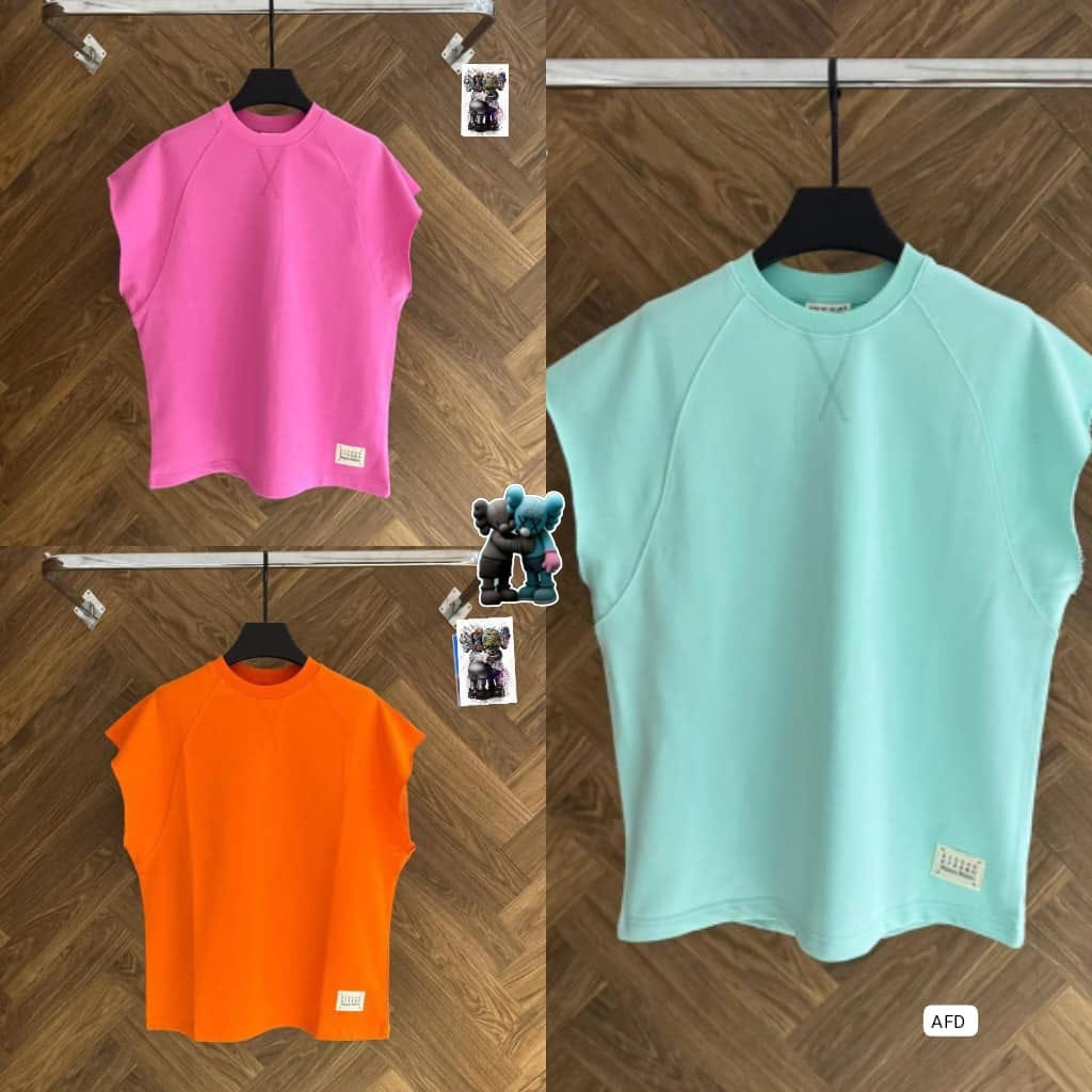 Sleeveless unisex tops in pink, orange and light blue colors hanging on racks against wood floor.