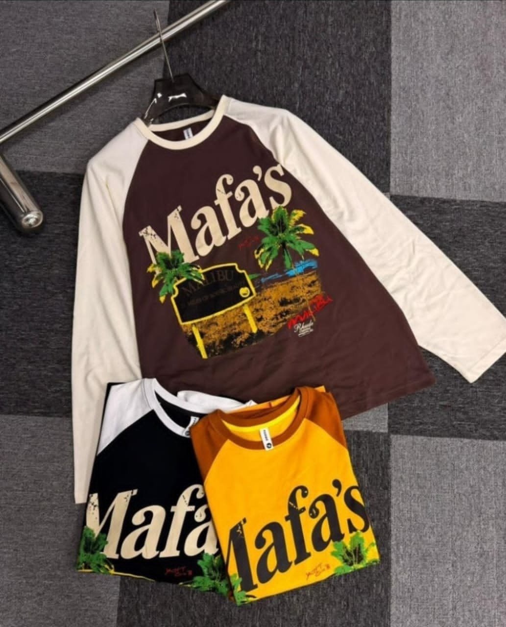 Three Mafa's graphic long sleeve raglan tees in brown, black and yellow colorways laid flat.